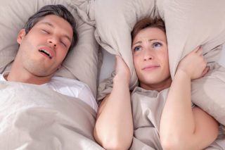 Woman covering her ears with pillow due to partner snoring