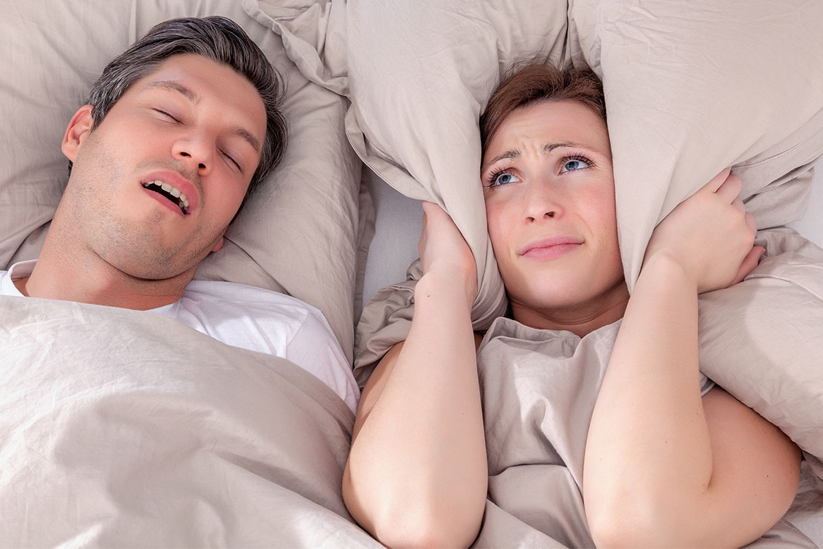 Woman covering her ears with pillow due to partner snoring